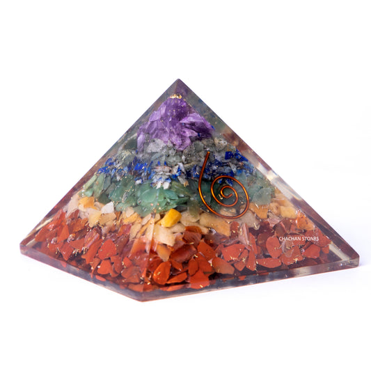 Pyramid-shaped crystal with colorful stones and a copper coil on a white background
