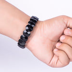 Black beaded bracelet on a wrist with a plain background
