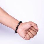 Hand wearing a black beaded bracelet on a white background