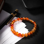 Orange beaded bracelet on a dark surface with a pen and paper