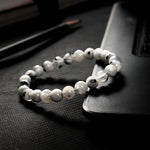 White beaded bracelet on a dark textured surface with 'Stardust Stones' branding.