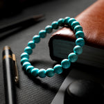 Turquoise beaded bracelet on a dark surface with a pen and book in the background