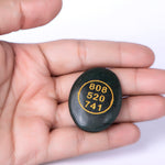 Black stone with yellow text held in a hand against a white background