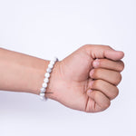 Hand wearing a white beaded bracelet on a light purple background