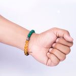 Hand wearing a bracelet with green and yellow beads on a light gray background