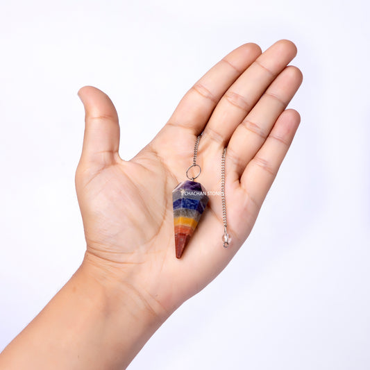 Hand holding a rainbow-colored 7 chakra dowser against a white background