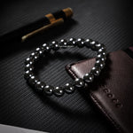 Black beaded bracelet on a textured black surface with a pen in the background