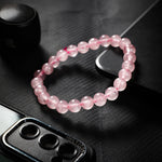 Pink beaded bracelet on a black textured surface with a JBL speaker in the background.