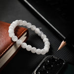White beaded bracelet on a dark surface with a book and pencil