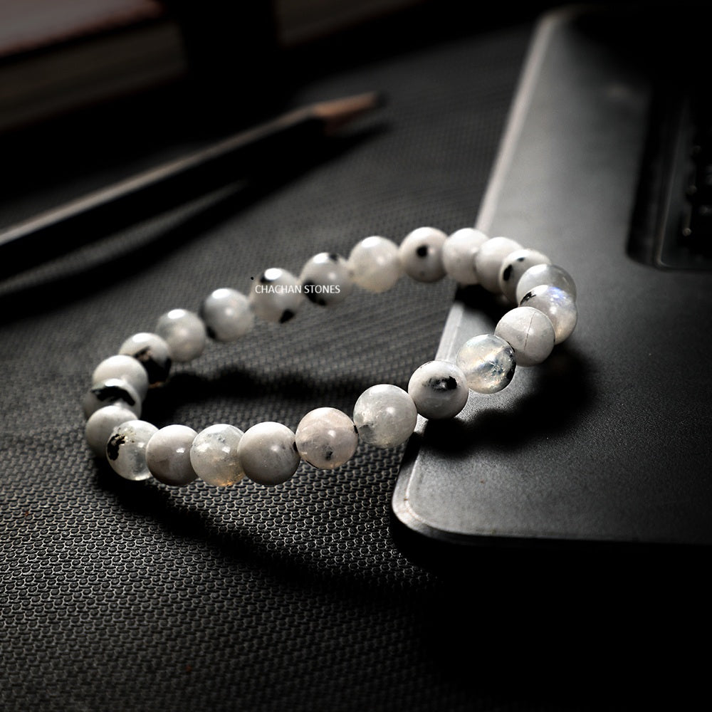White beaded bracelet on a dark textured surface with 'Stardust Stones' branding.