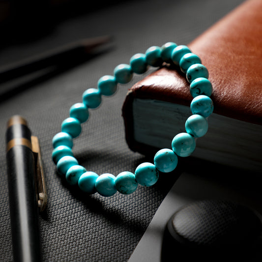 Turquoise beaded bracelet on a dark surface with a pen and book in the background
