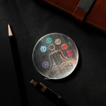 Circular artwork with a figure and colorful symbols on a dark surface with a pencil.