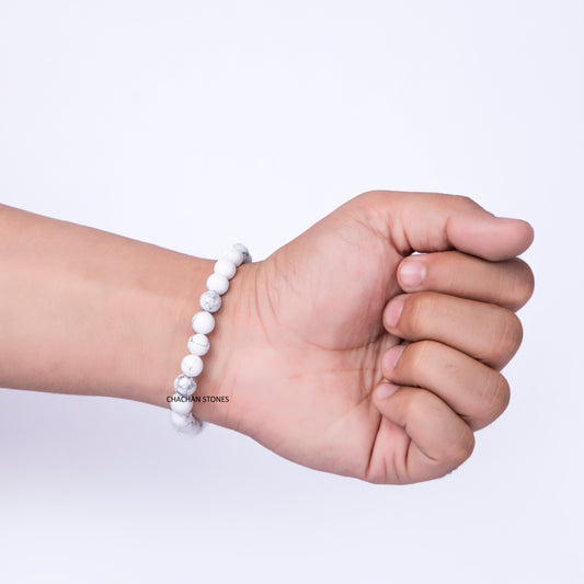 Hand wearing a white beaded bracelet on a light purple background